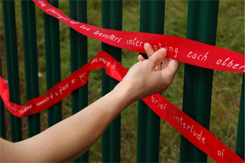 photograph of a hand holding embroidered ribbon attached to green railings